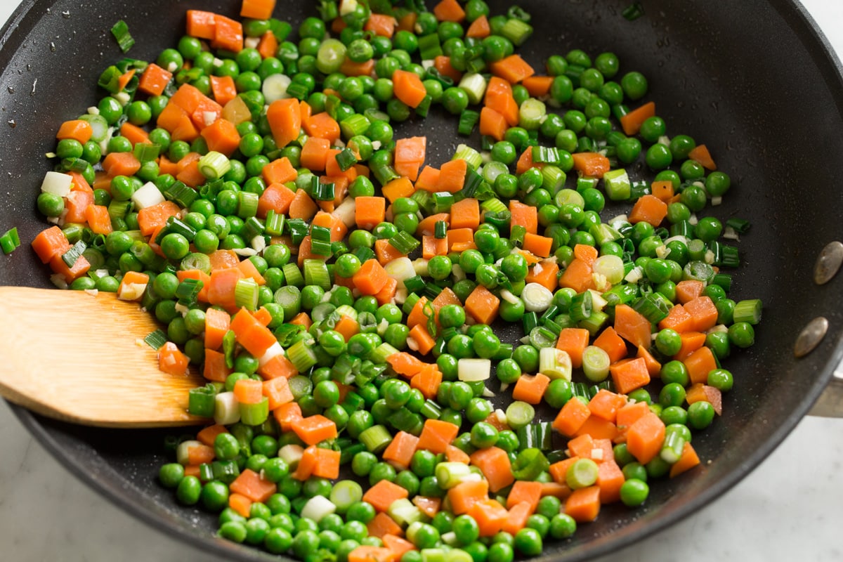 Sautéing peas and carrots in skillet for fried rice.
