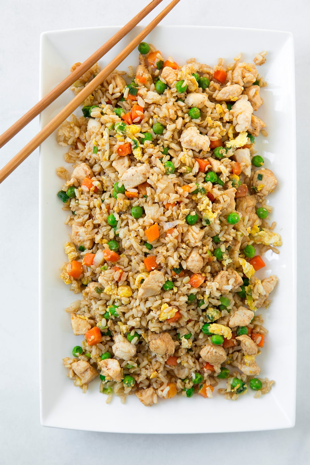 An overhead image of chicken fried rice on a white platter with chop sticks on the side.