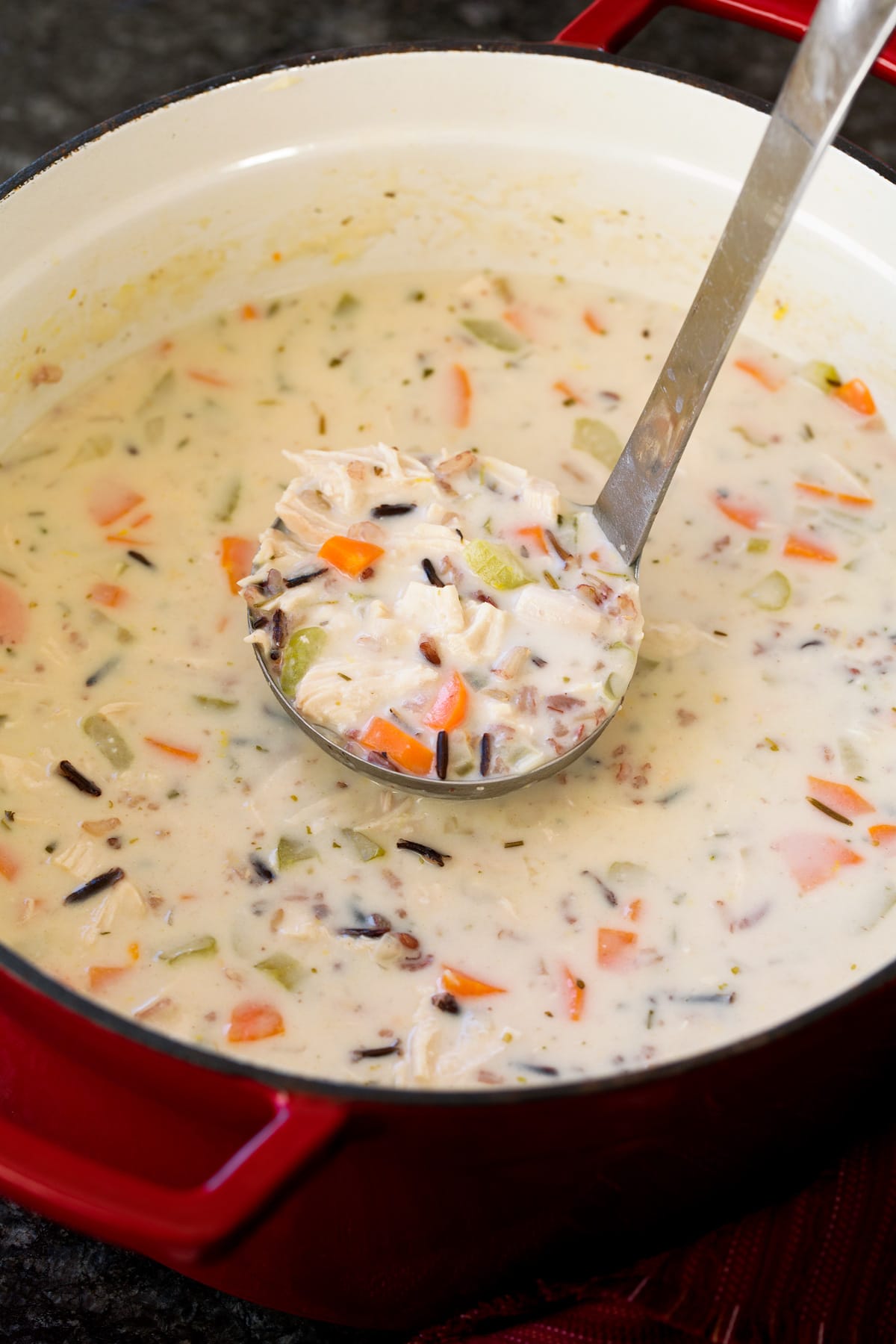 Chicken and wild rice soup in a pot with ladle full being scooped out. 