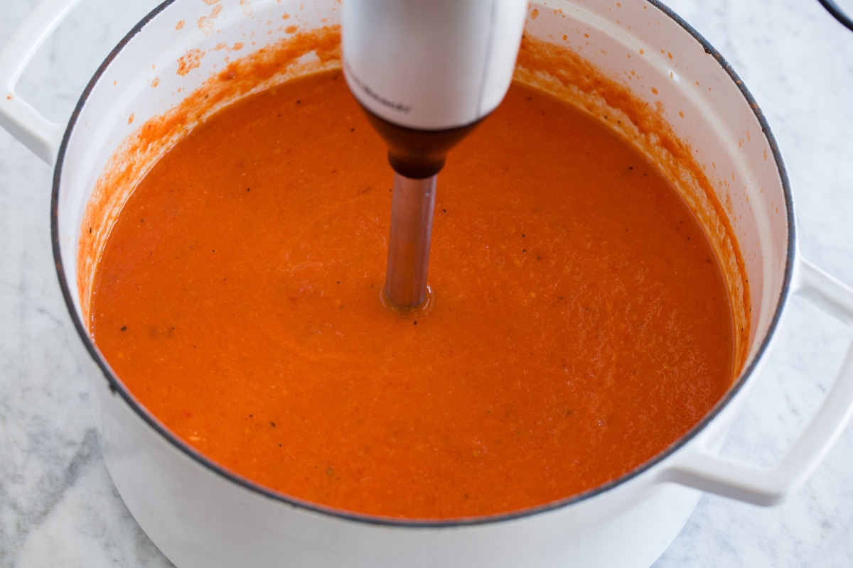 Roasted tomato basil soup being blended in a pot with an immersion blender.