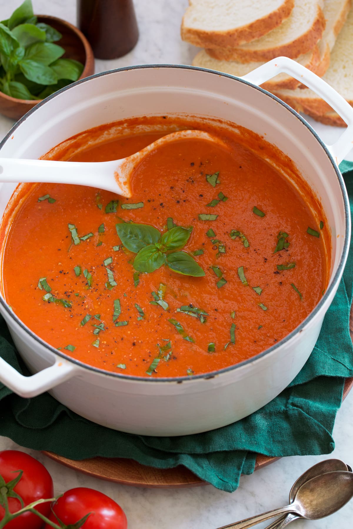 White pot filled with roasted tomato basil soup on a green cloth.