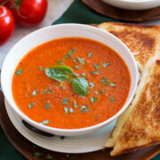 Servire la zuppa di pomodoro e basilico mostrata da vicino in una ciotola bianca con un formaggio grigliato a lato.