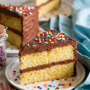 Slice of homemade yellow cake with chocolate frosting and sprinkles.