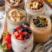 Overnight oats in mason jars, five different ways, on a wooden platter next to a spoon.
