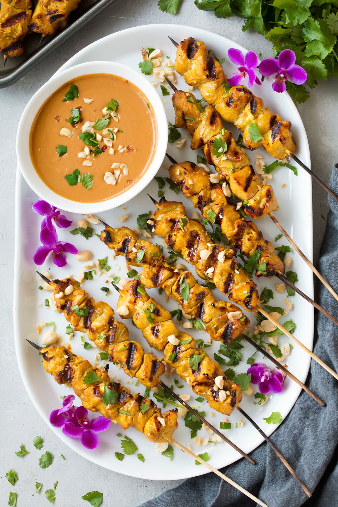 Chicken Satay skewers on white platter with bowl of peanut satay sauce