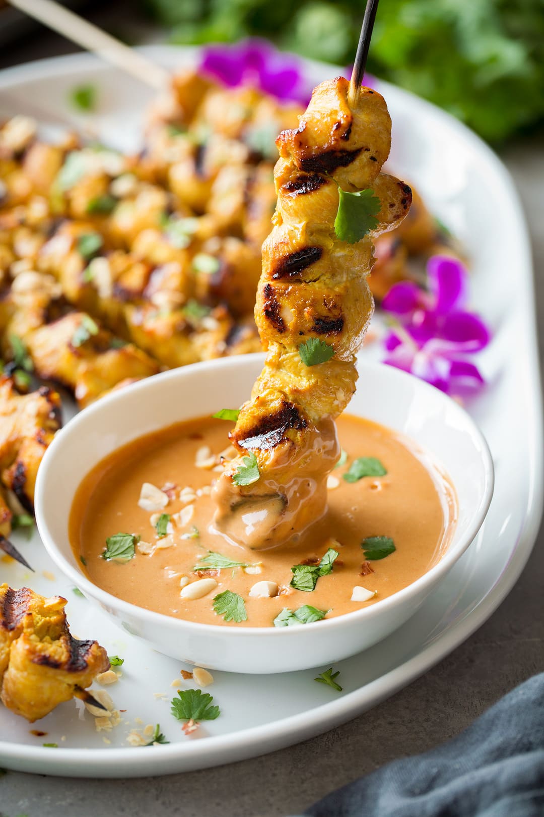 thai chicken satay skewer being dipped into bowl of peanut sauce