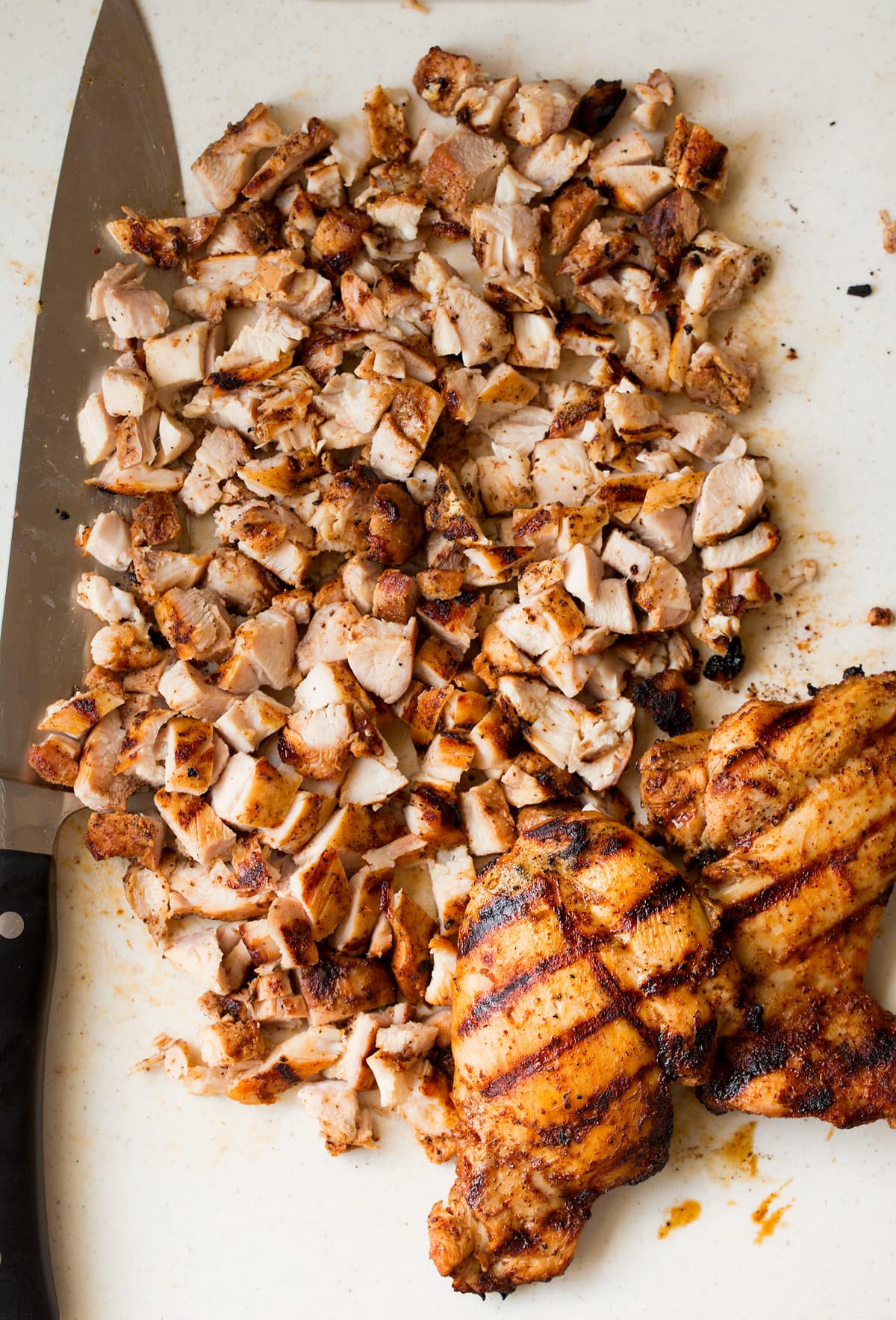 Chicken being diced on a cutting board into small pieces to serve in tacos.