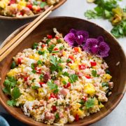 Wooden bowl full of hawaiian fried rice decorated with flowers and chopsticks to the side.