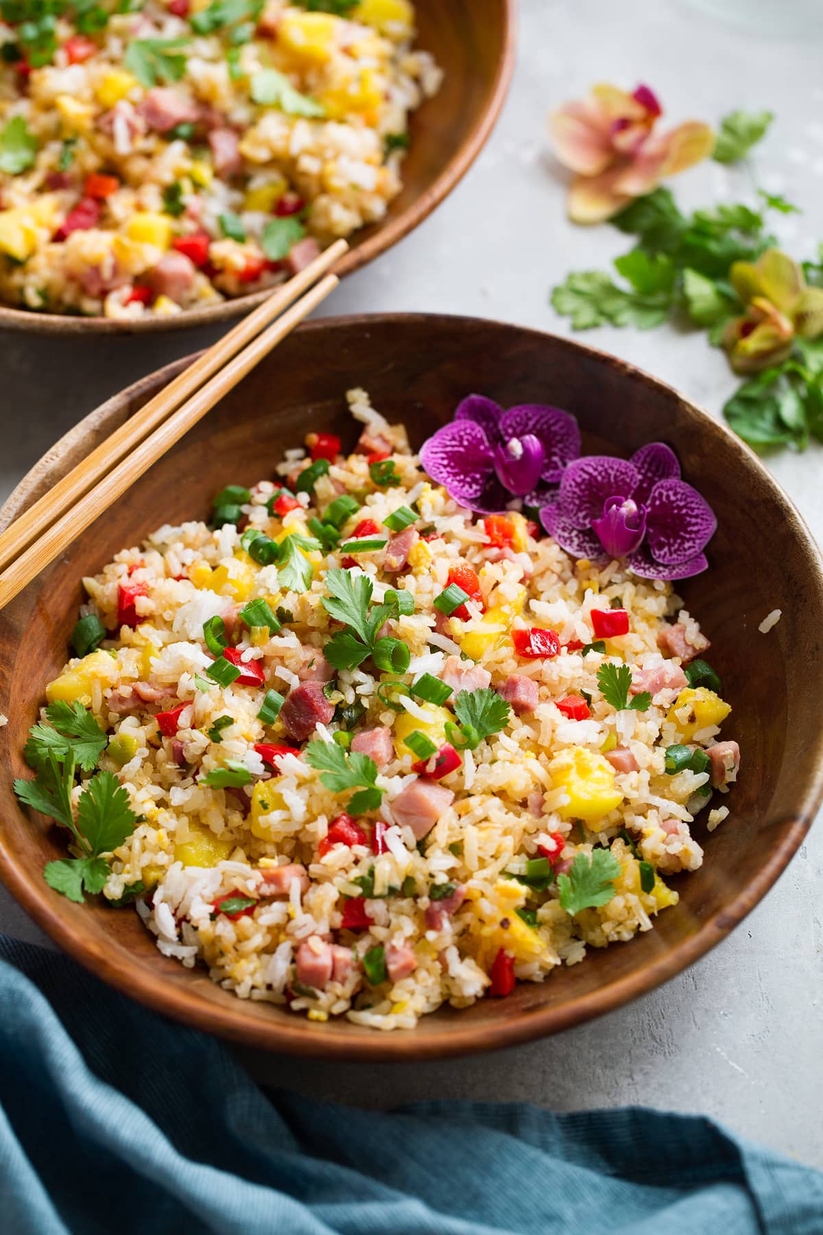 Wooden bowl full of hawaiian fried rice decorated with flowers and chopsticks to the side.