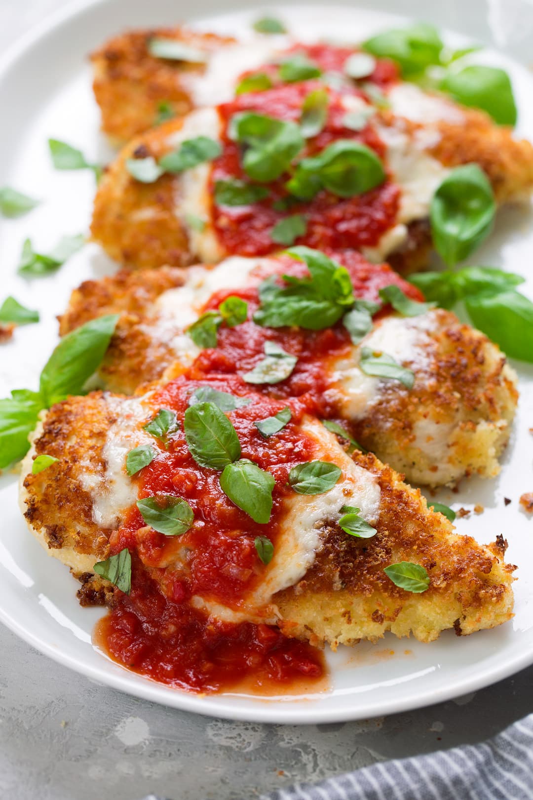 Row of four pieces of chicken parmesan on a white serving platter.