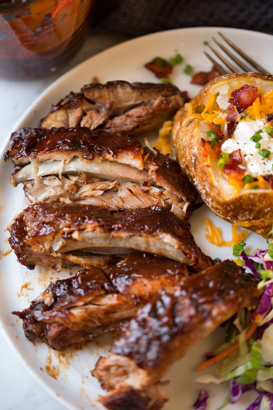 Tender slow cooker ribs on plate with loaded baked potato and coleslaw
