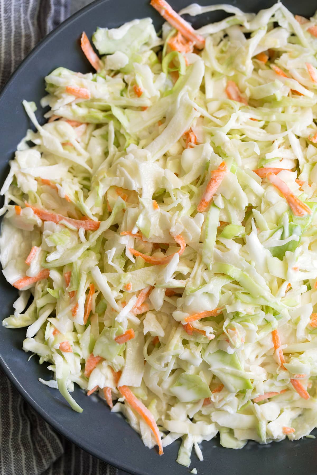 Close up image of coleslaw with dressing in a dark blue bowl.