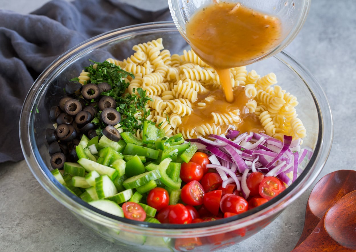 Greek Pasta Salad pouring dressing over salad ingredients