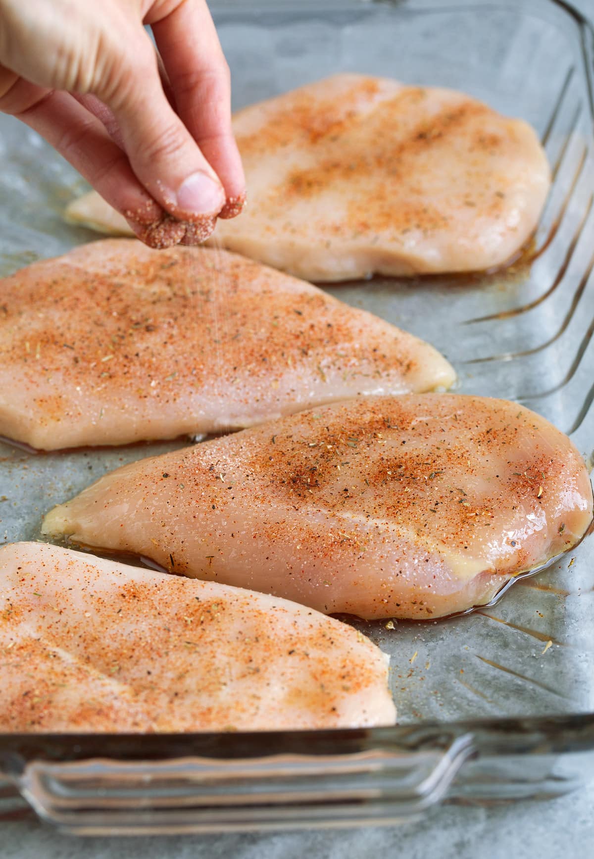 Sprinkling seasoning mixture over raw chicken breasts in glass baking dish before baking. 