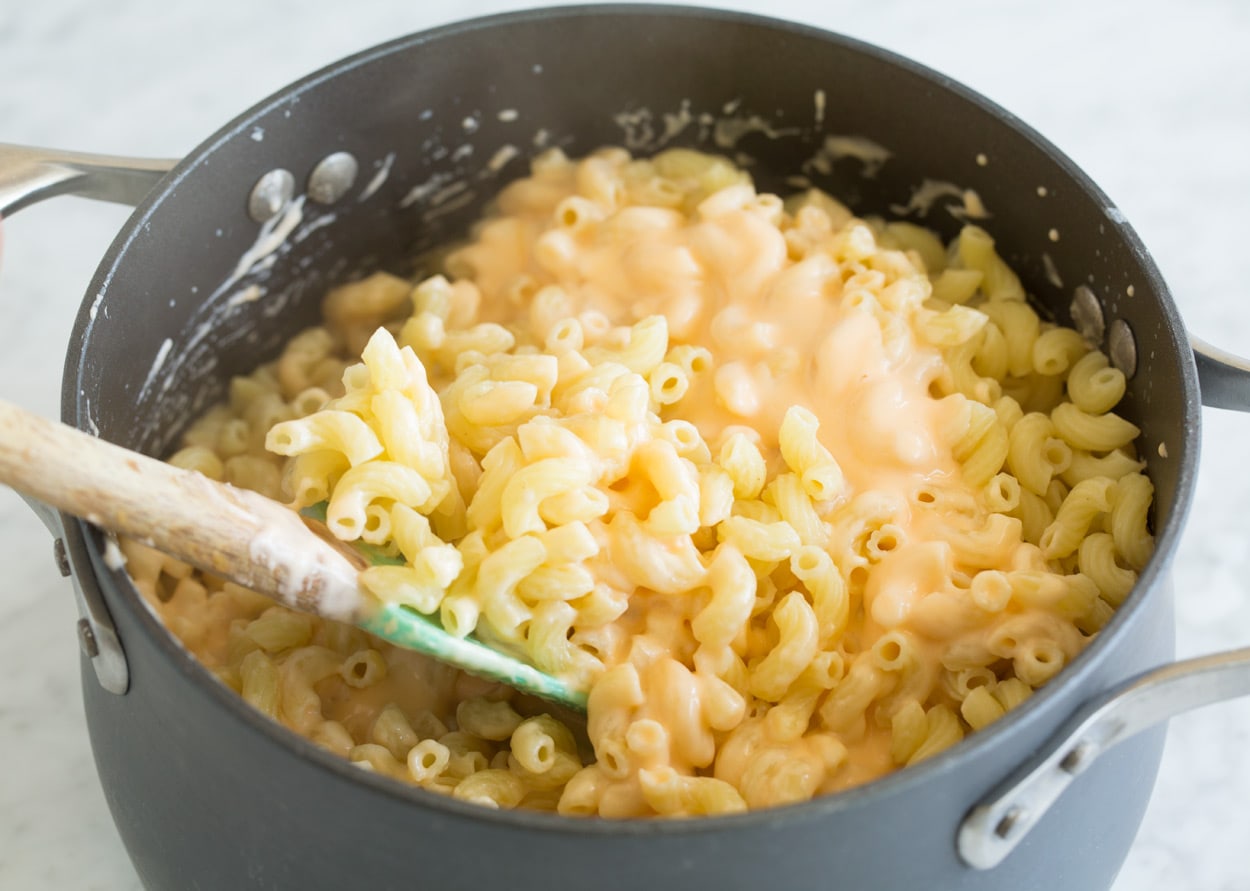Tossing cooked pasta with mac and cheese sauce in pot.