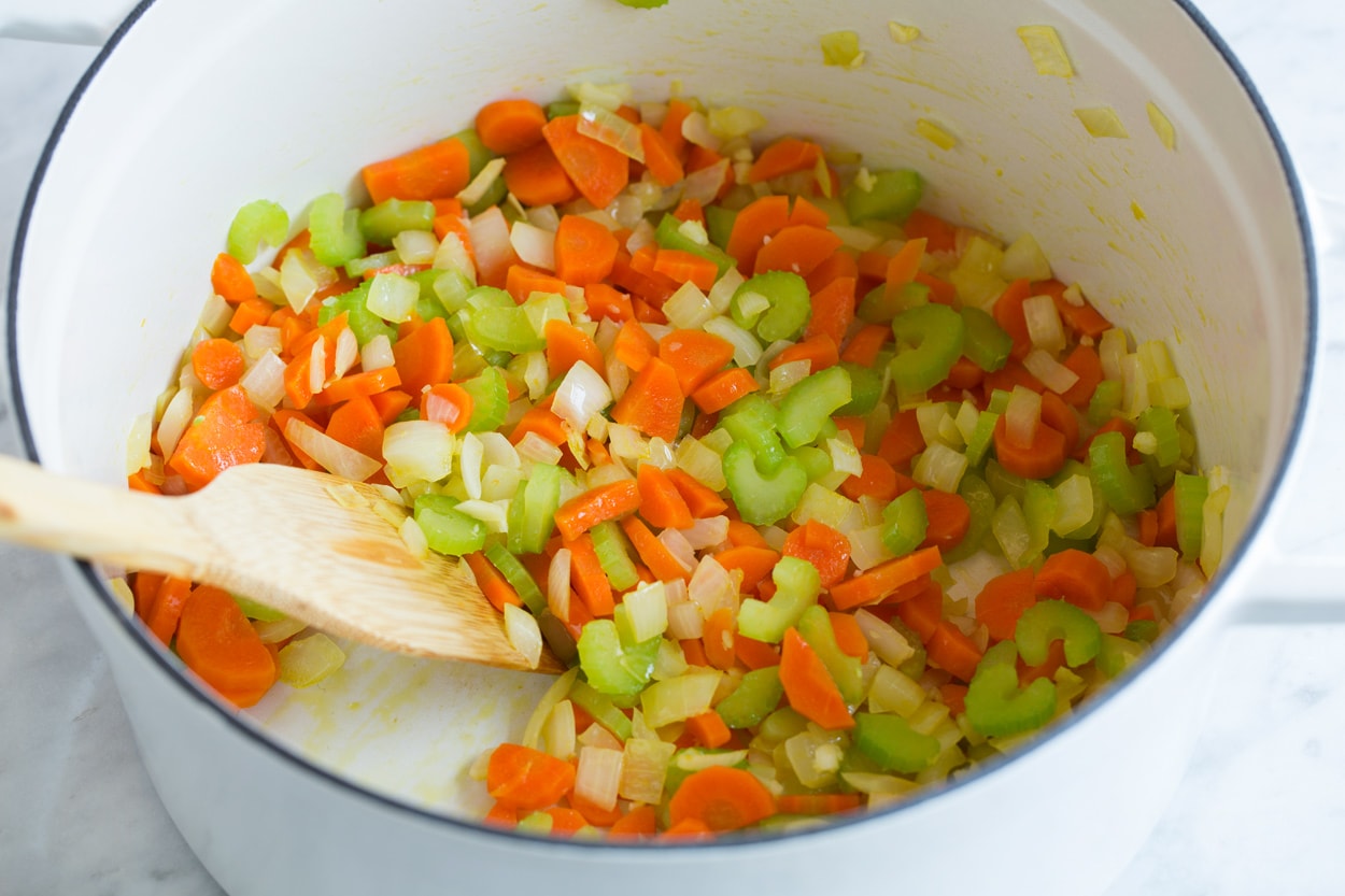 Showing how to make cabbage soup. Sauteeing carrots, onions and celery in a large white pot.