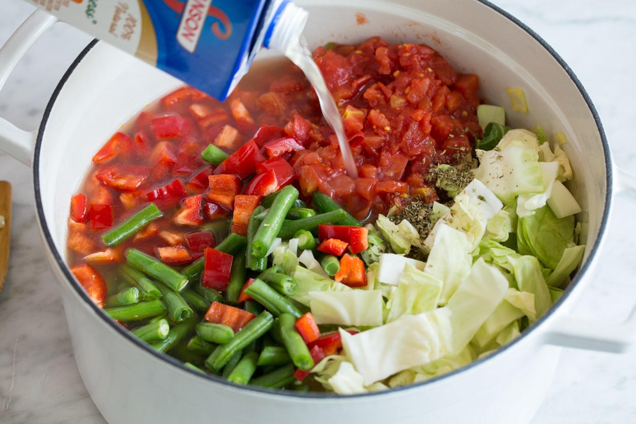 Adding cabbage, tomatoes, green beans, chicken broth and seasoning to soup mixture.