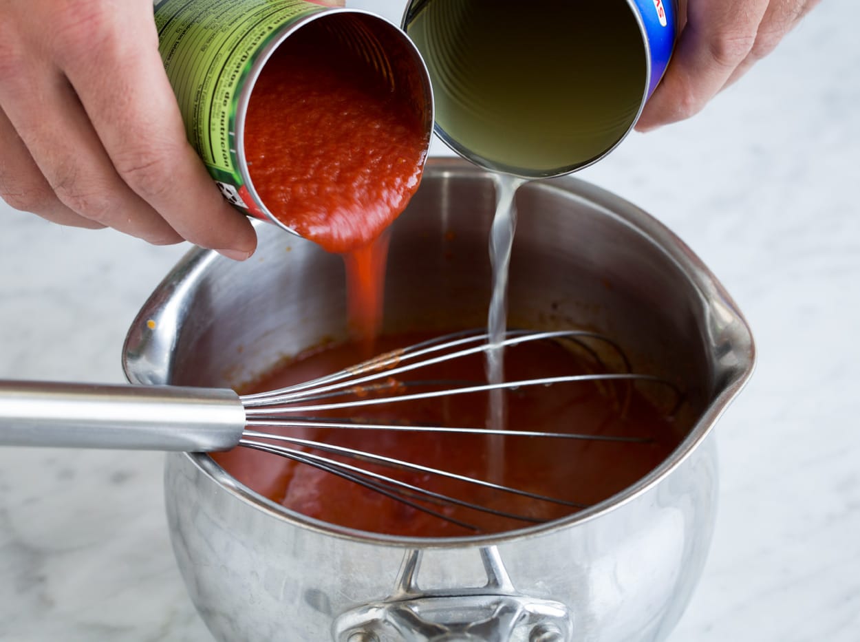 adding tomato sauce and broth to pot of Enchilada Sauce