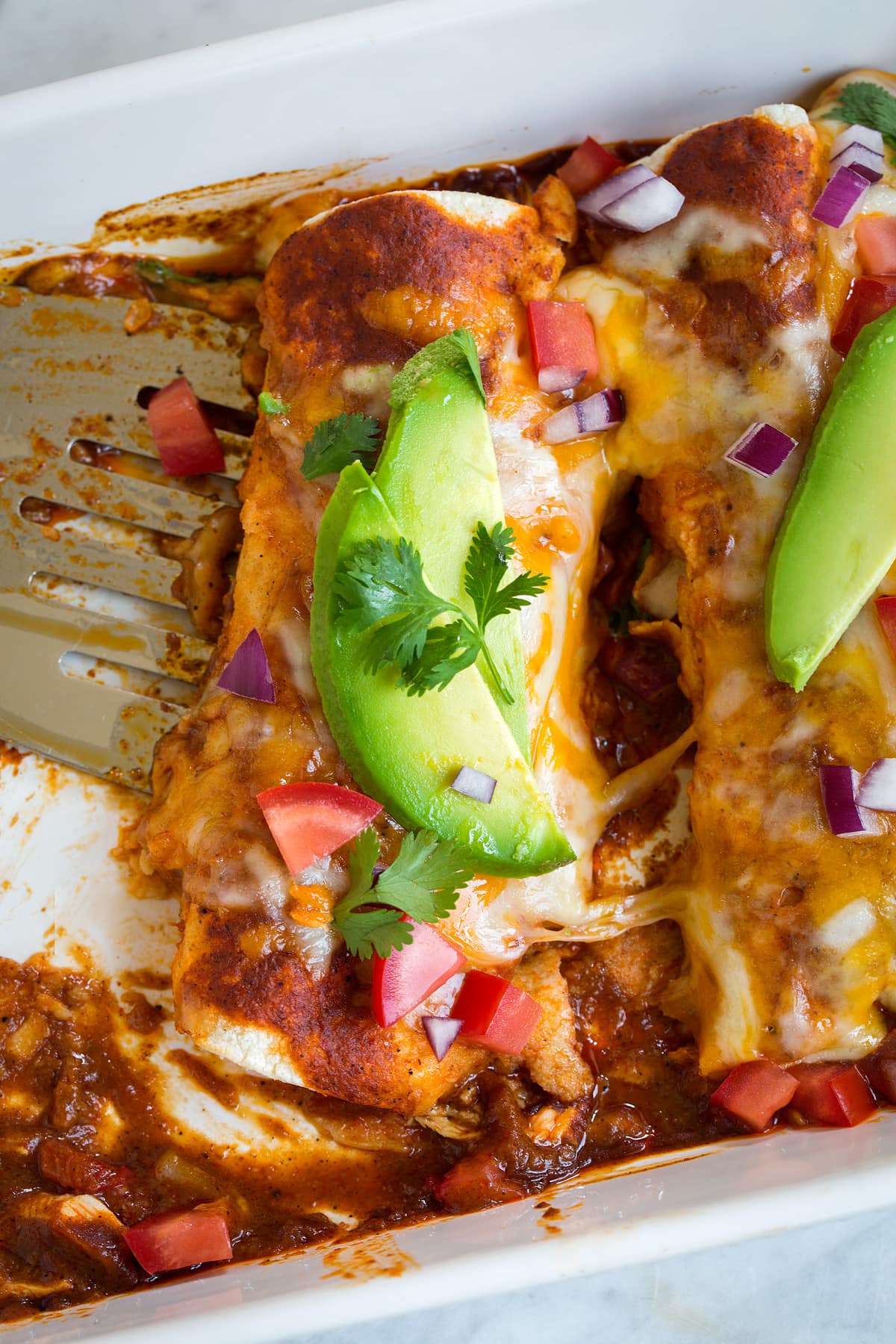 removing a mexican chicken enchilada from white baking dish with a spatula