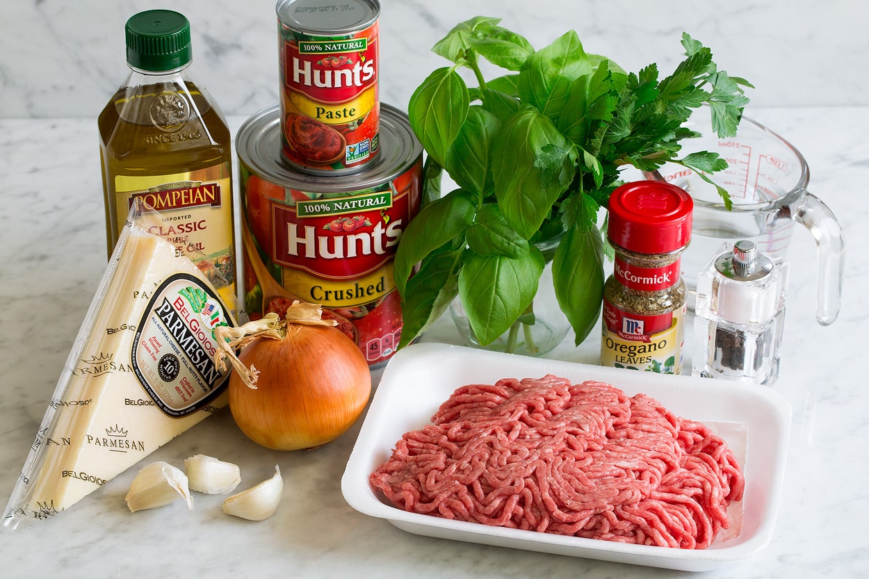 Spaghetti Sauce ingredients shown here including ground beef, olive oil, salt, pepper, fresh basil, fresh parsley, dried oregano, onion, garlic, crushed tomatoes, tomato paste and parmesan.