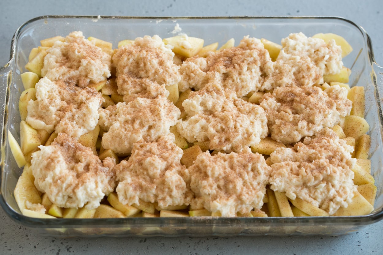 Apple cobbler shown here adding biscuit topping over apples in baking dish