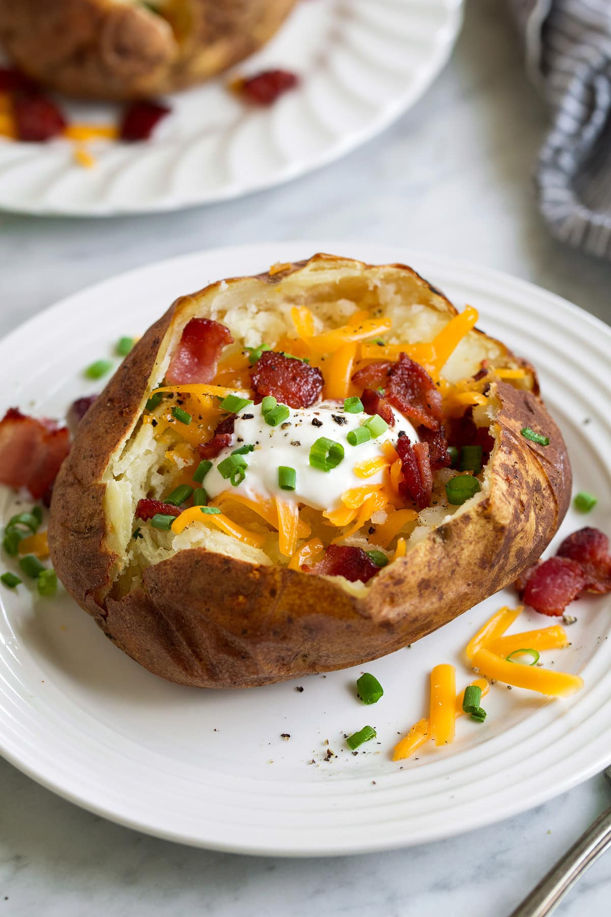 best baked potato topped with sour cream cheese bacon and chives on white plate
