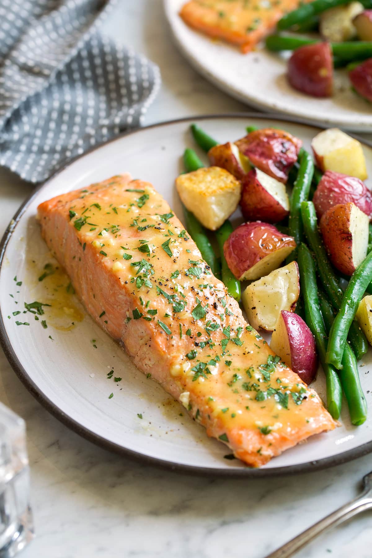 Single baked salmon fillet on a serving dish with a side of roasted potatoes and carrots. Salmon is brushed with a honey mustard sauce.