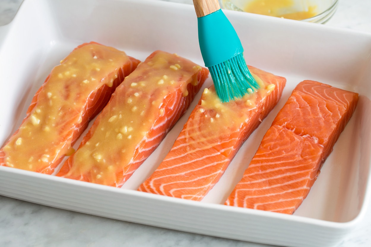 Showing how to make baked salmon. Brushing four fillets in baking dish with honey mustard sauce.