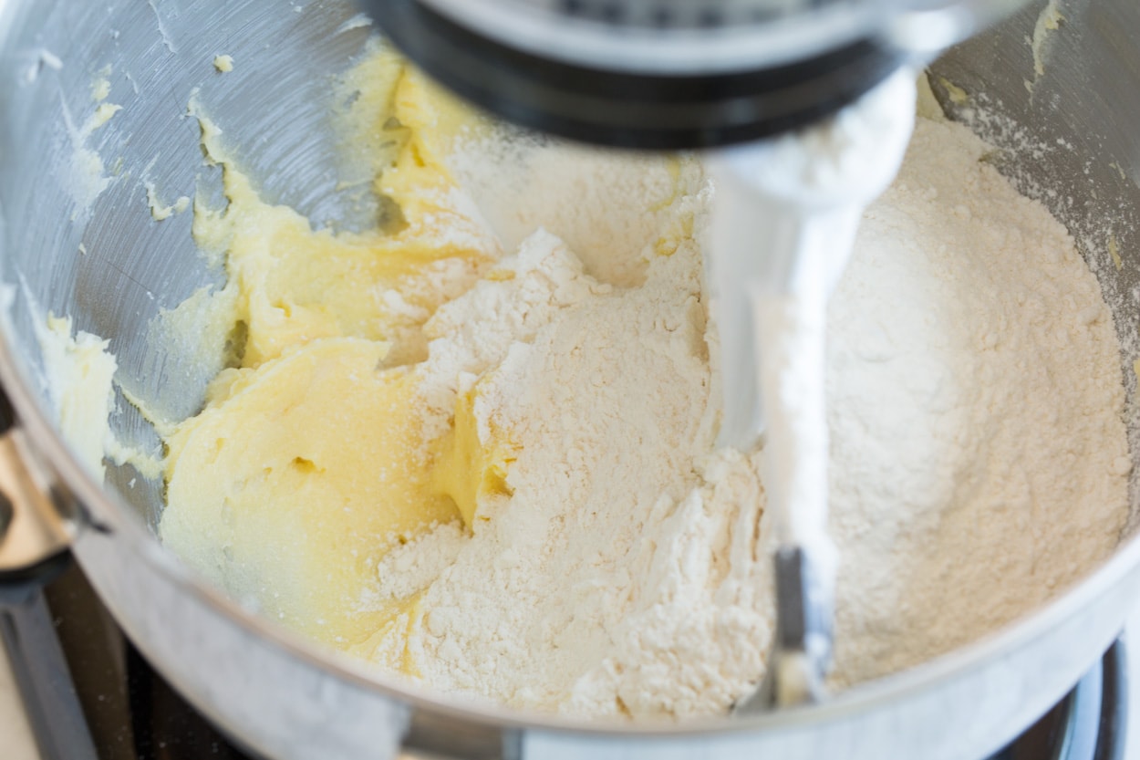 Adding flour to butter cookie mixture in stand mixer.