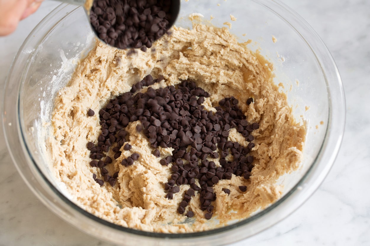 Adding chocolate chips to cookie dough in mixing bowl