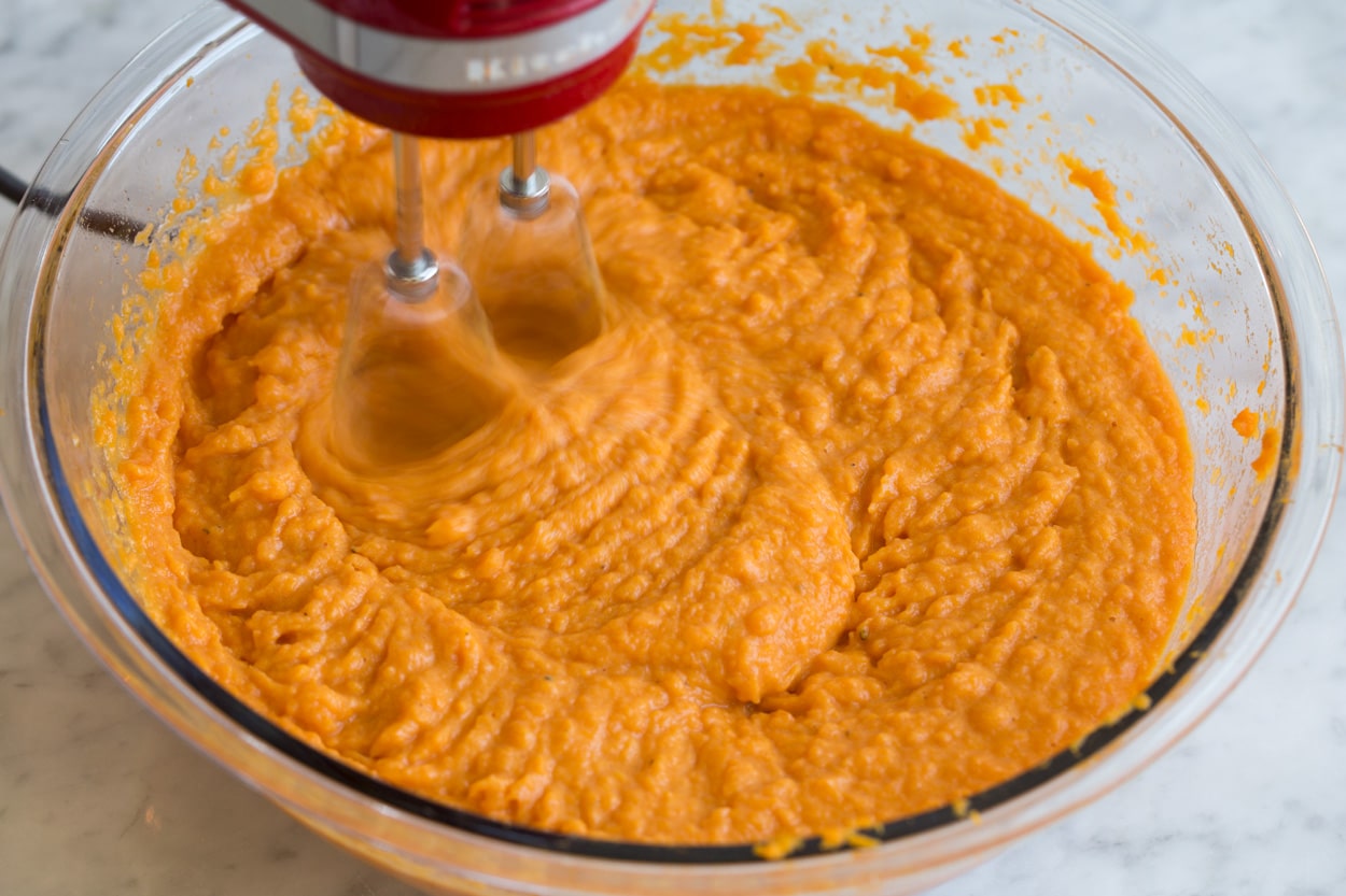 Mixing sweet potato mixture in glass mixing bowl with electric hand mixer, for sweet potato casserole. 