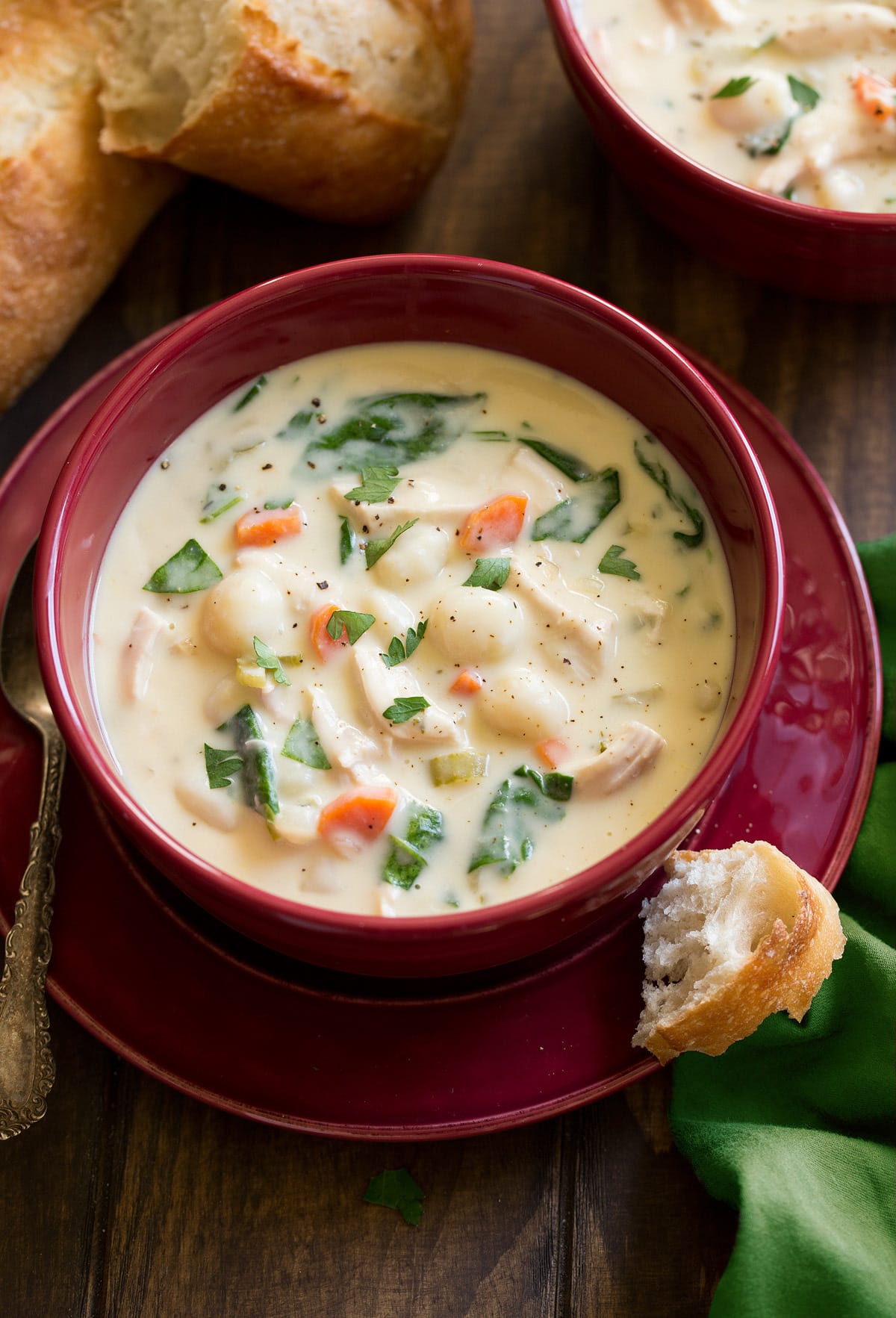 Serving of creamy chicken gnocchi soup in a red soup bowl.