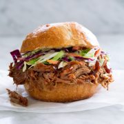 Pulled Pork shown here in a bun with coleslaw sitting on parchment paper on a marble surface