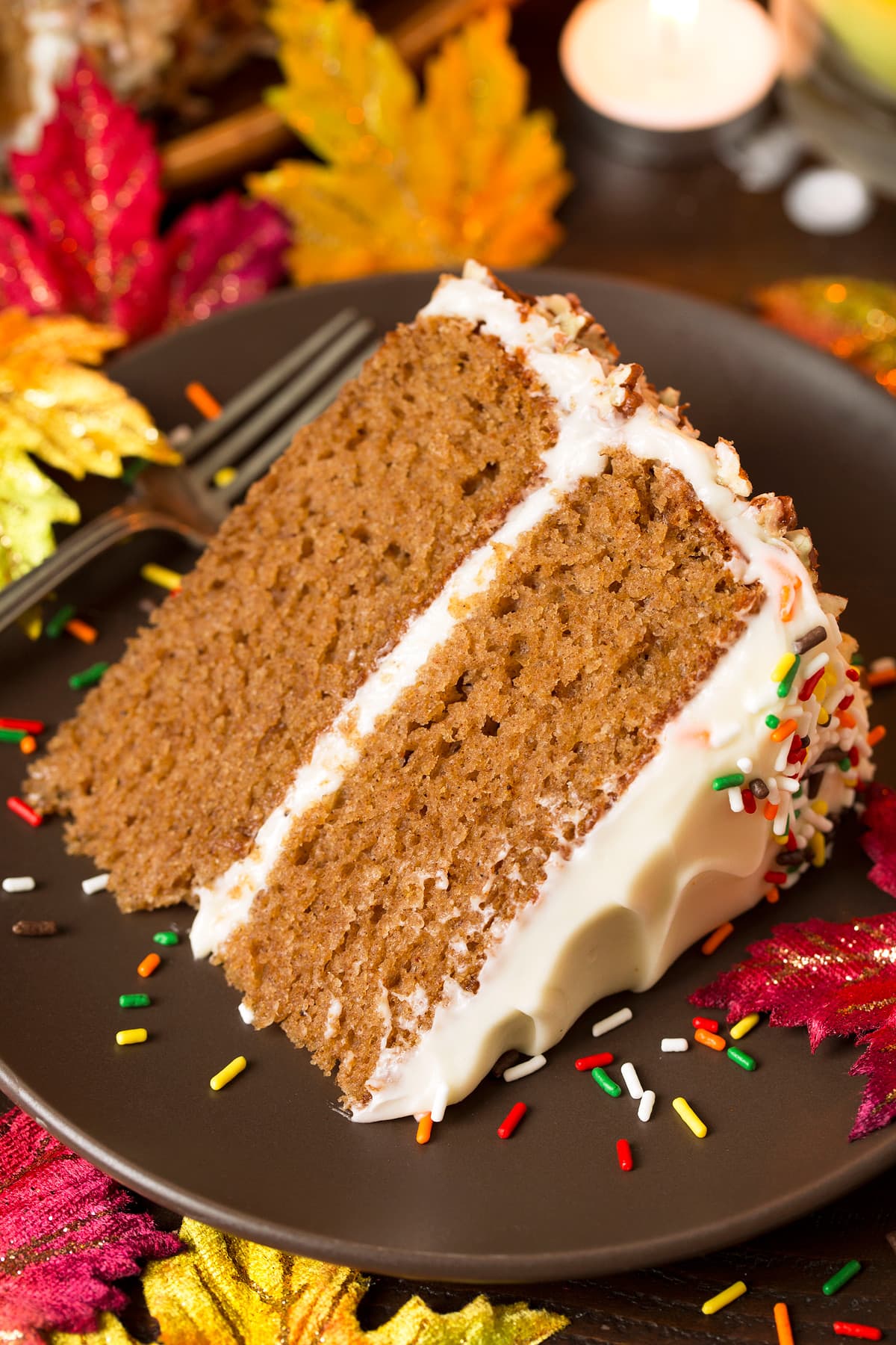 Spice Cake slice with cream cheese frosting, on a brown matte plate decorated with colorful fall leaves around it.