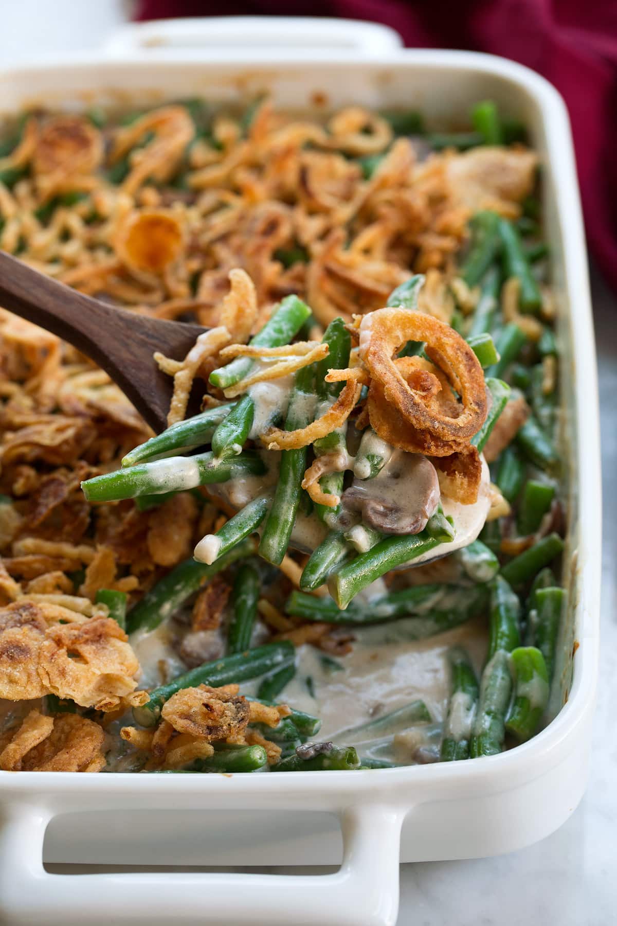 Close up image of a scoop of green bean casserole. Fresh green beans are coated with a creamy mushroom filling and topped with French's fried onions. 