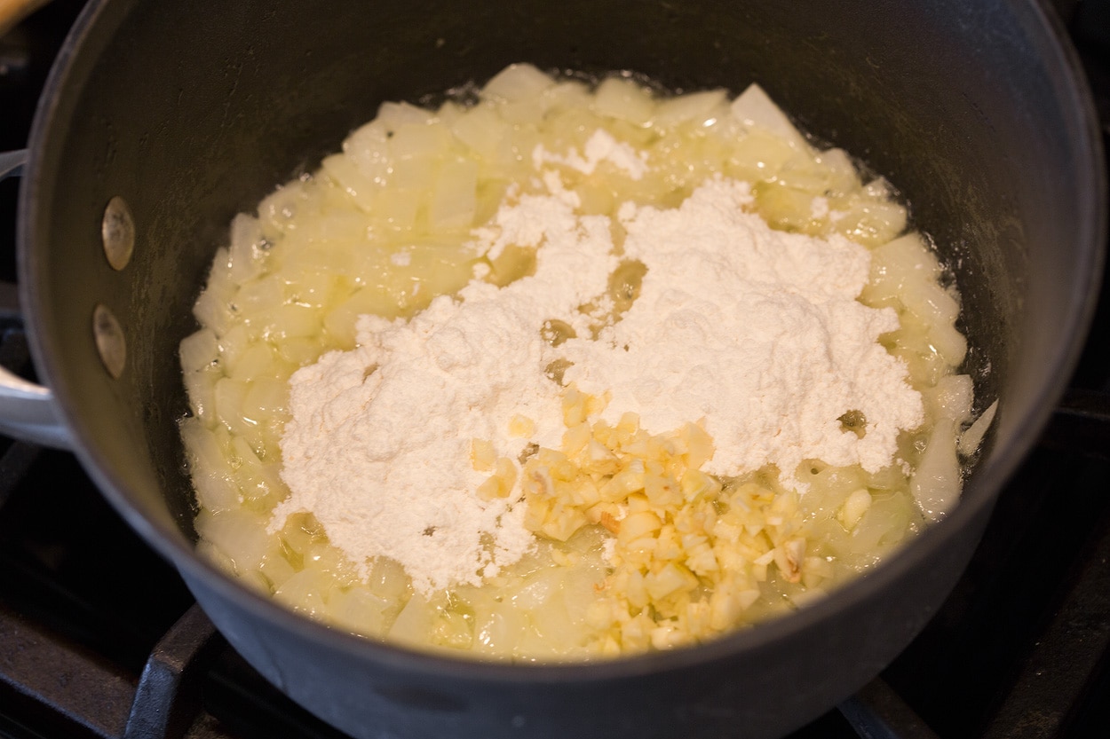 Showing how to make scalloped potatoes, starting with sauteing onion, garlic, and flour in butter in a medium saucepan.