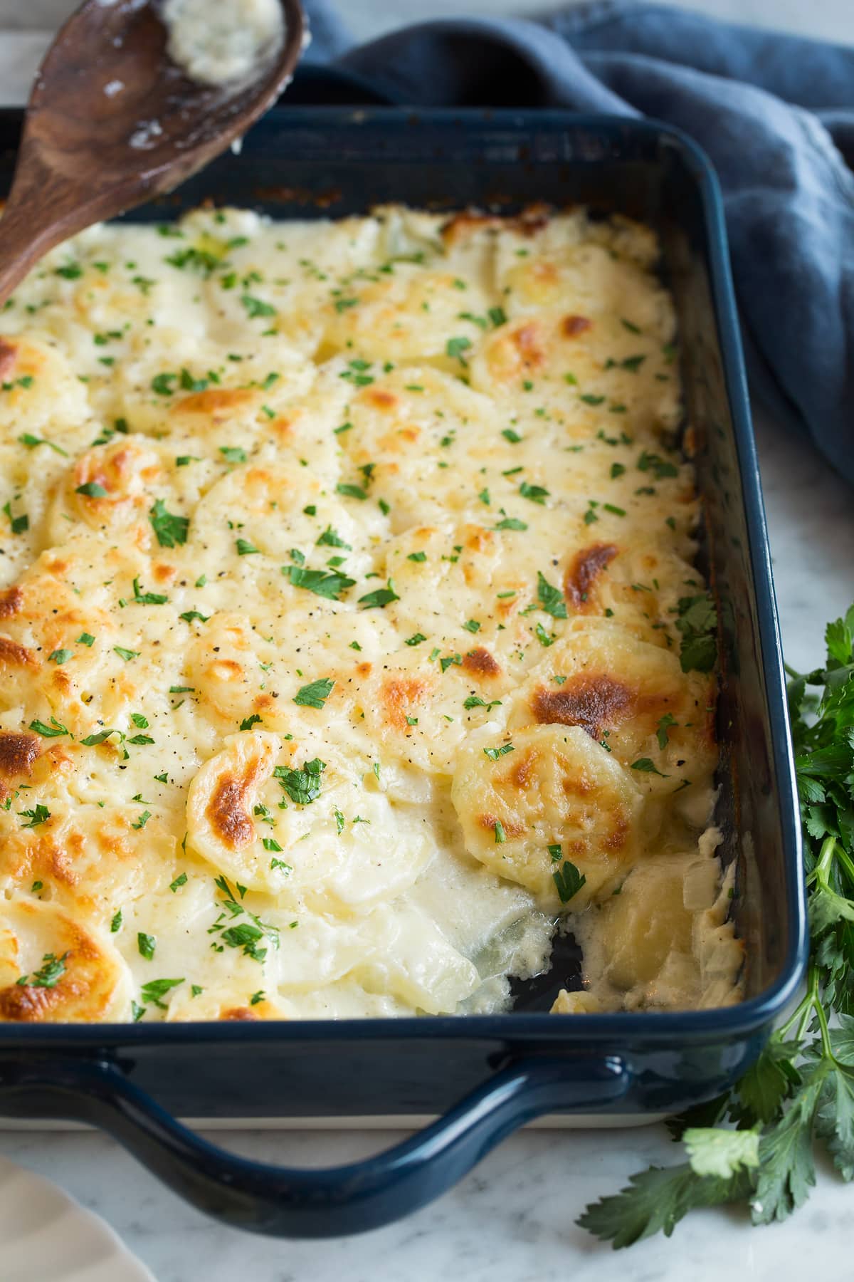 Scalloped Potatoes in a navy 13 by 9 inch baking dish set over a marble surface.