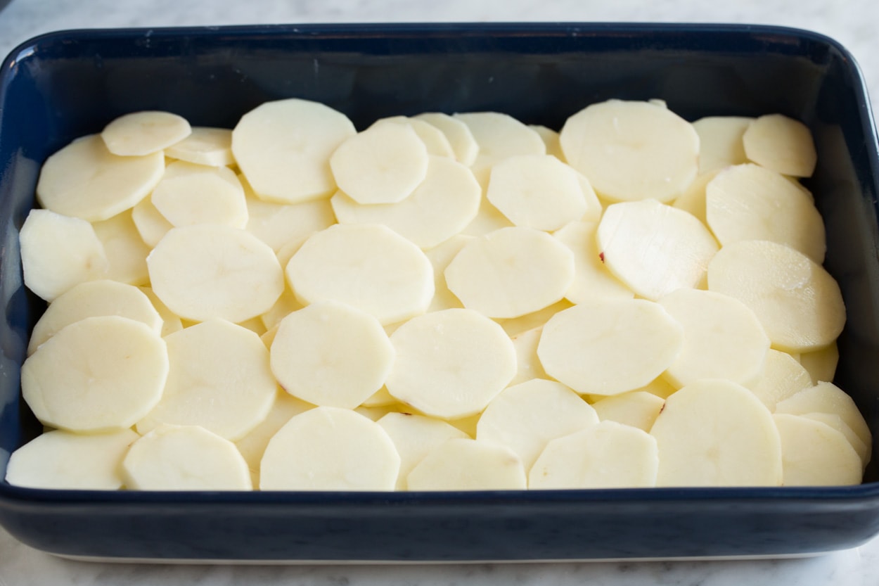 Spreading a second layer of thinly sliced potatoes over sauce layer in baking dish for scalloped potatoes.