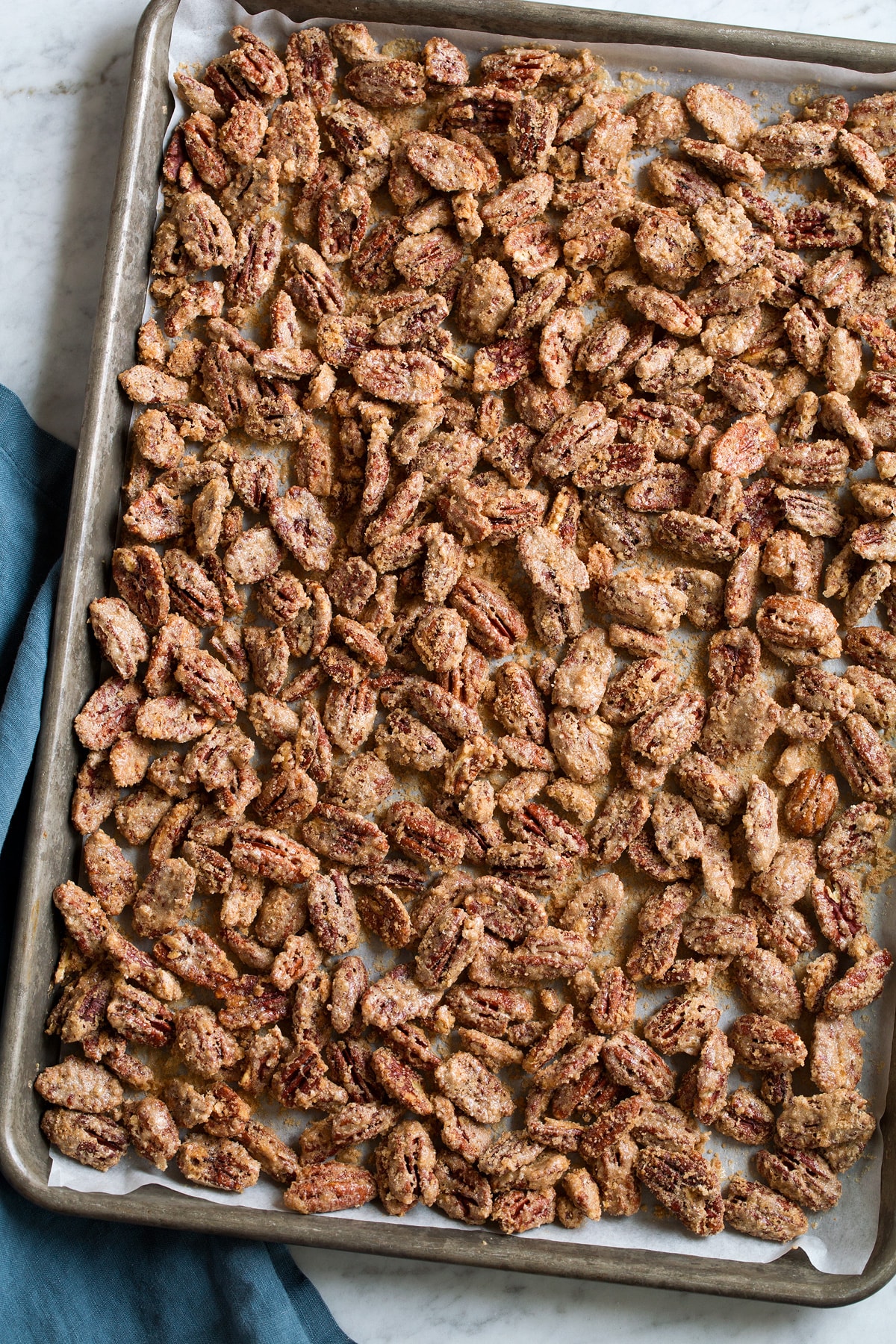 Finished candied pecans on a parchment paper lined baking sheet. 