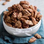 Candied pecans mounded high in a white bowl set over a blue cloth.