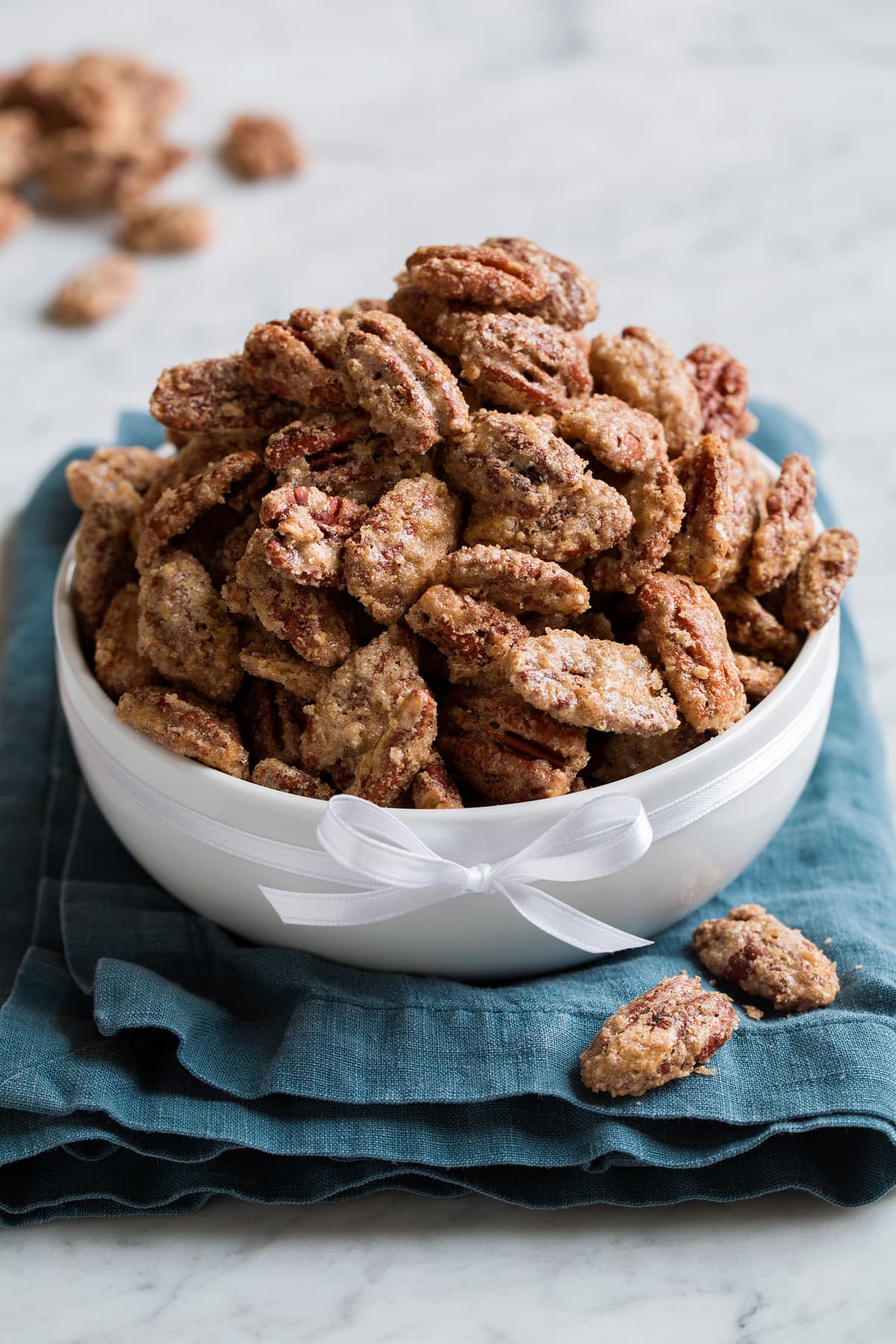 Candied pecans mounded high in a white bowl set over a blue cloth.