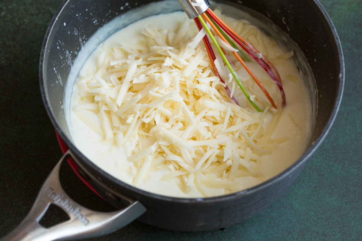 Adding cheese to milk mixture in saucepan.