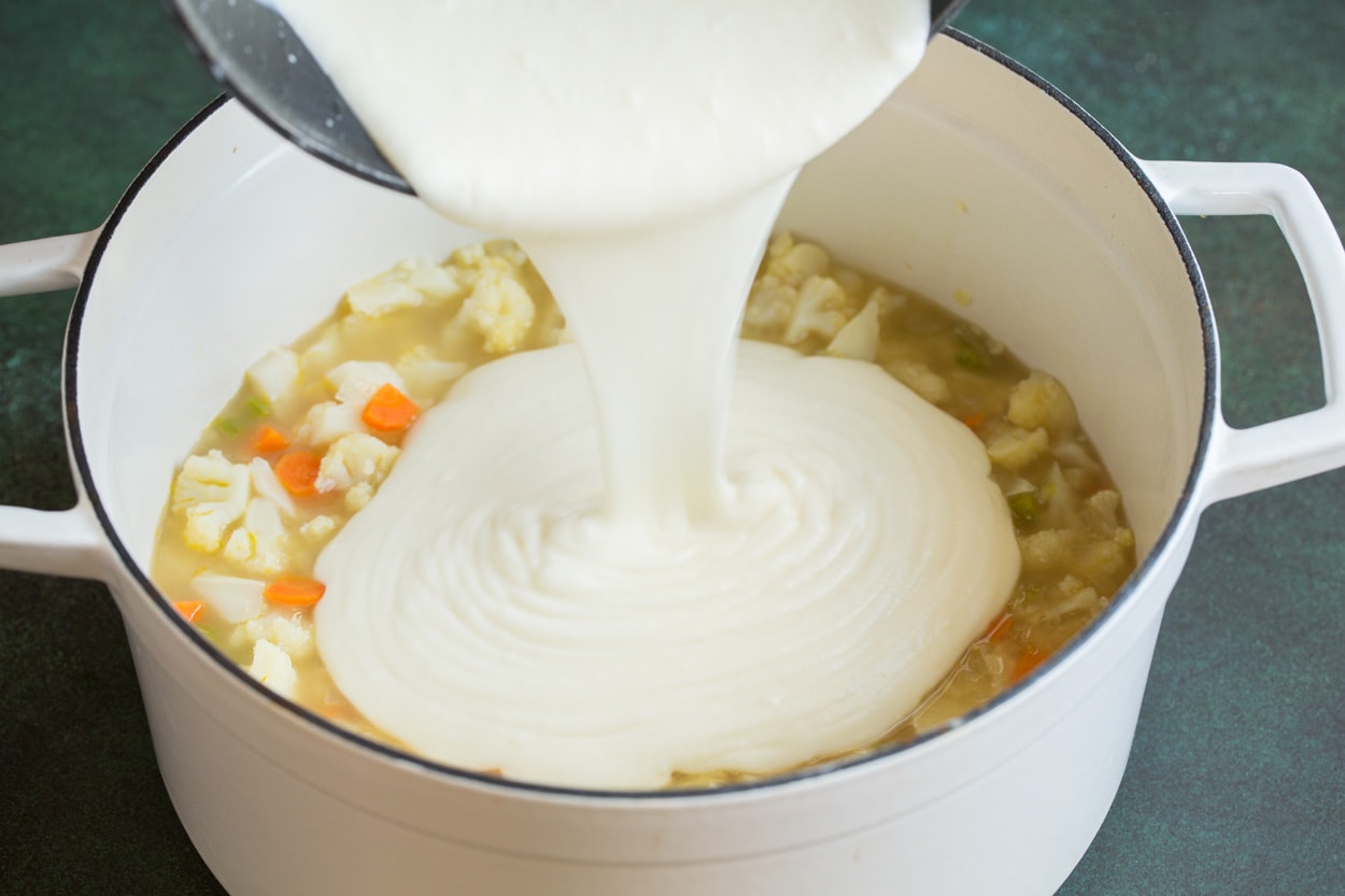 Pouring milk mixture into Cauliflower Soup in pot.