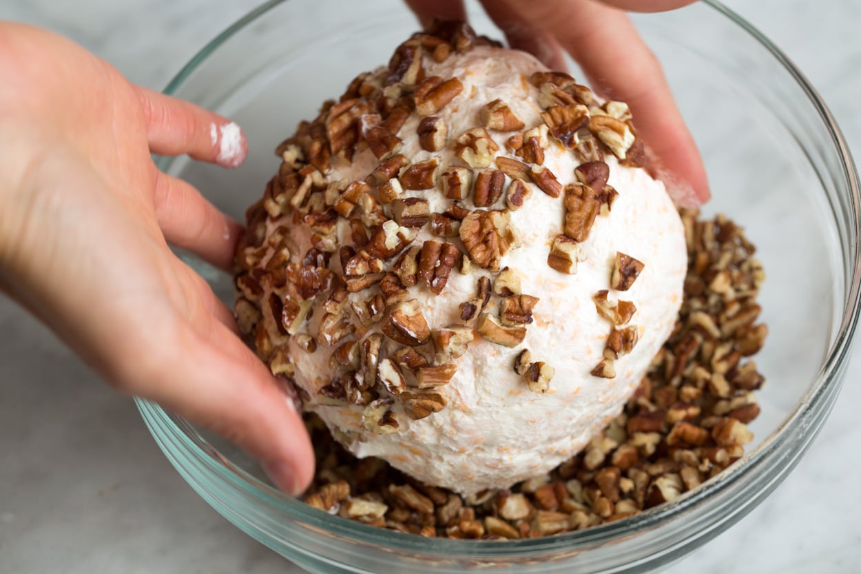 Rolling cheese ball through chopped pecans in a mixing bowl.