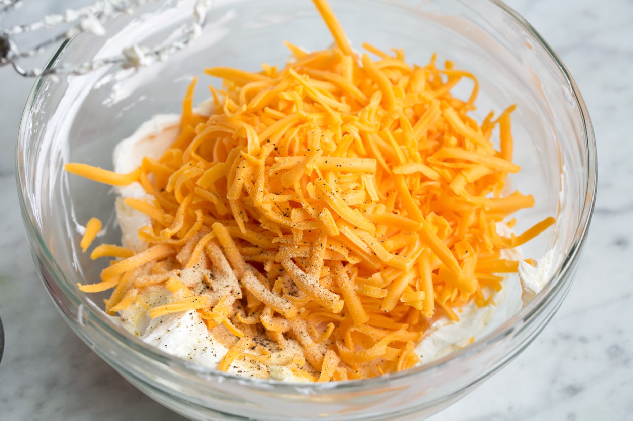 Mixing shredded cheddar into cheese ball mixture.