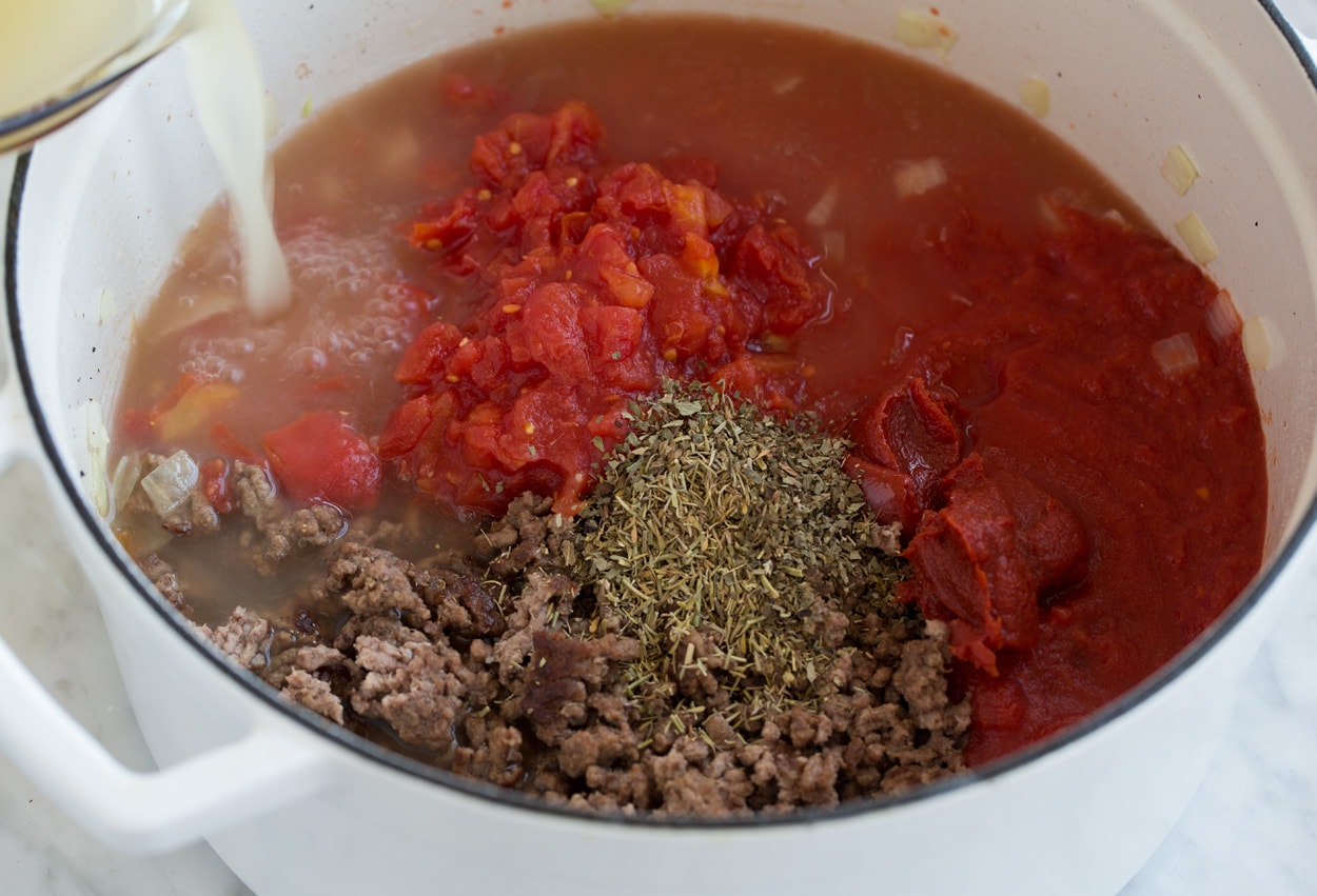 Adding broth, tomatoes and herbs to pot for lasagna soup.