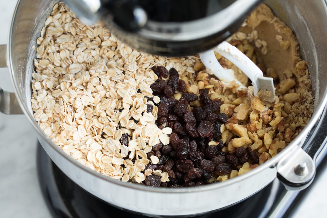 Adding oatmeal, raisins, walnuts to stand mixer to make oatmeal raisin cookies.