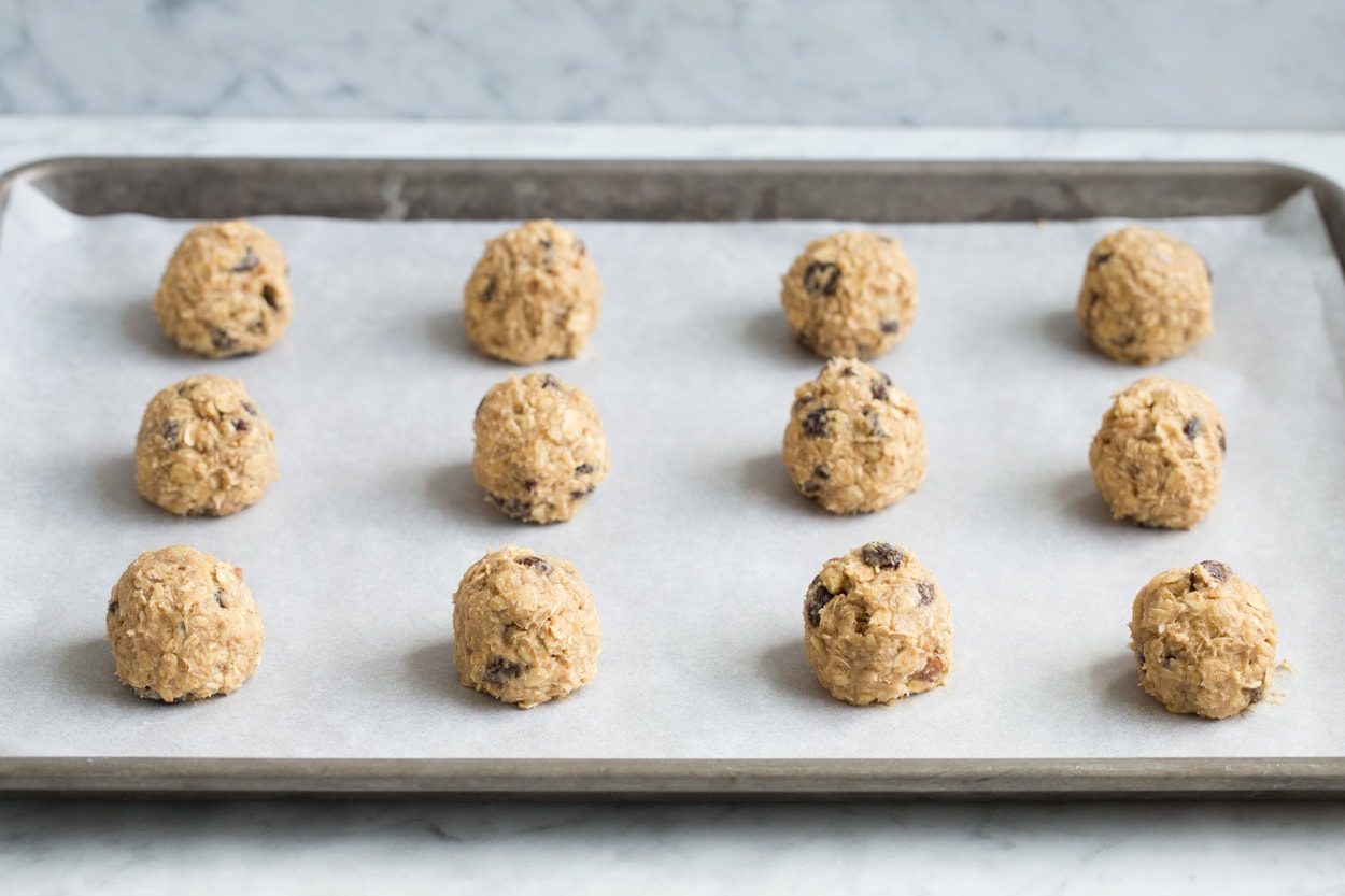 Oatmeal cookie dough balls on parchment paper lined baking sheet before baking.