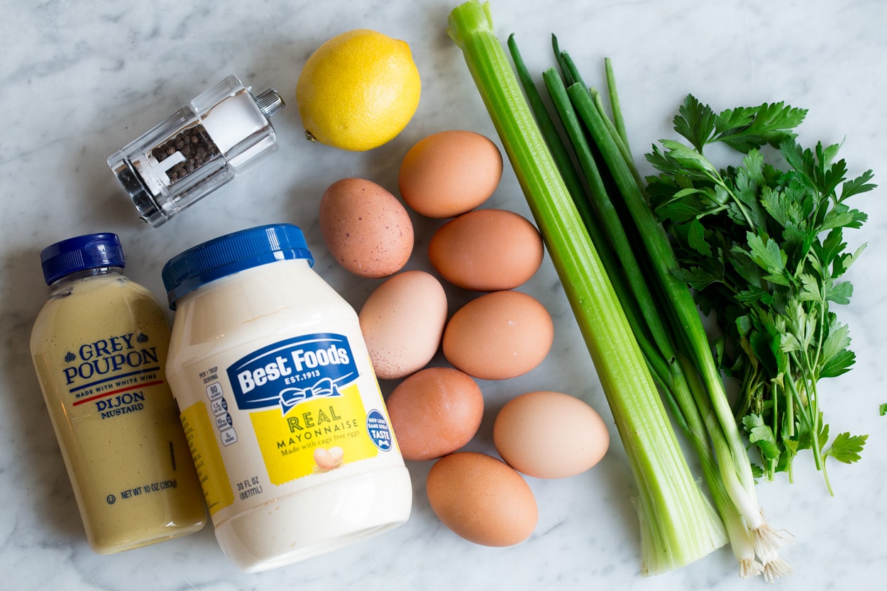 Ingredients needed for egg salad shown here including boiled eggs, mayonnaise, dijon, lemon, celery, green onions, parsley, salt and pepper.