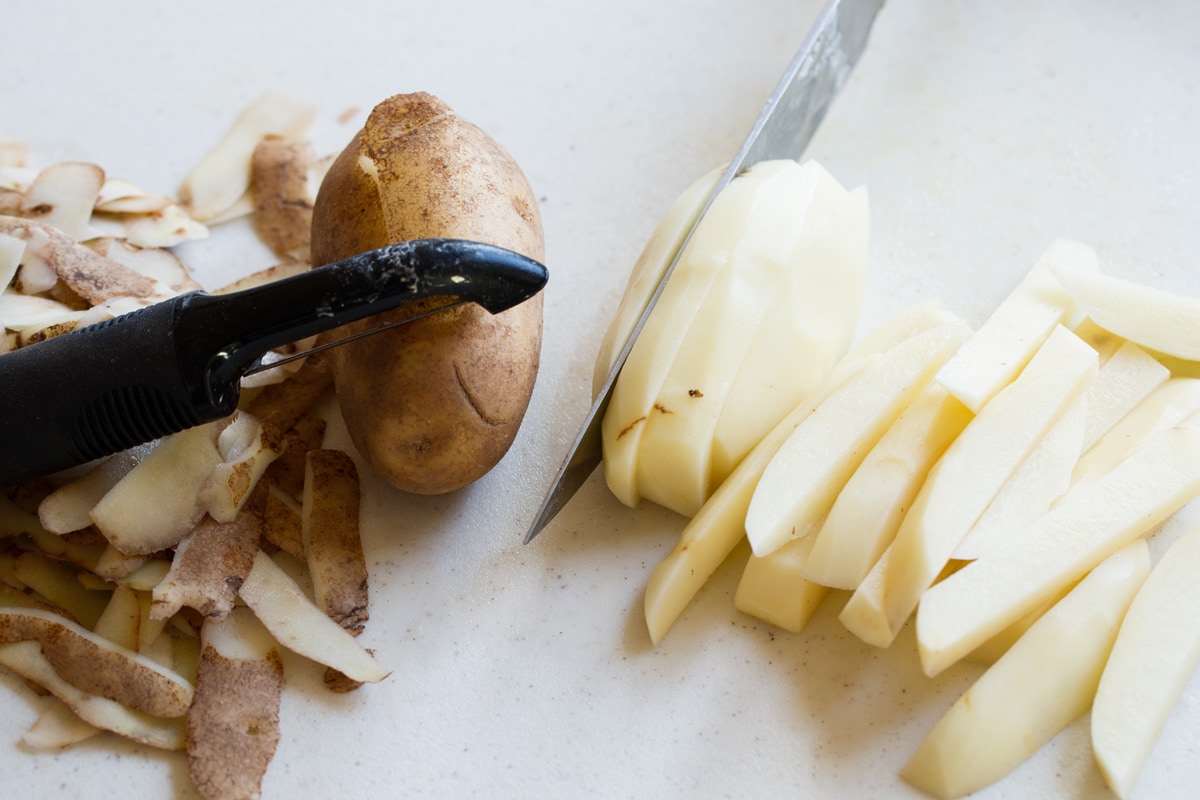 Showing how to prepare potatoes for french fries, peeling potatoes and slicing into sticks.